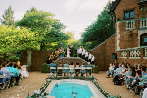 A bride and a groom stand at the top of brick stairs for a courtyard wedding ceremony at the Rollins Mansion Des Moines.