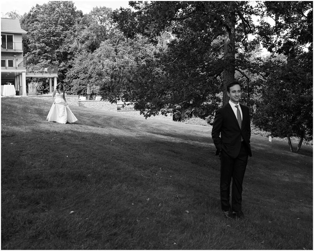 A bride walks across a lawn towards a groom for a first look.