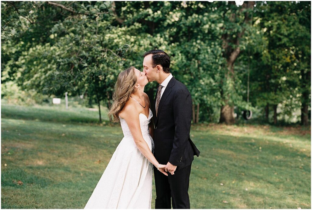 A bride and groom kiss on a lawn.