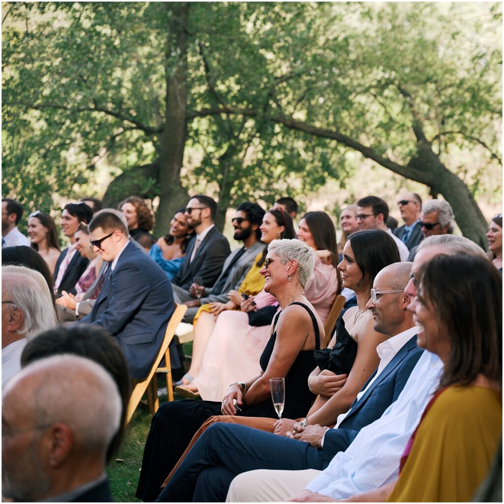 Wedding guests smile as they watch an outdoor wedding in Iowa City.