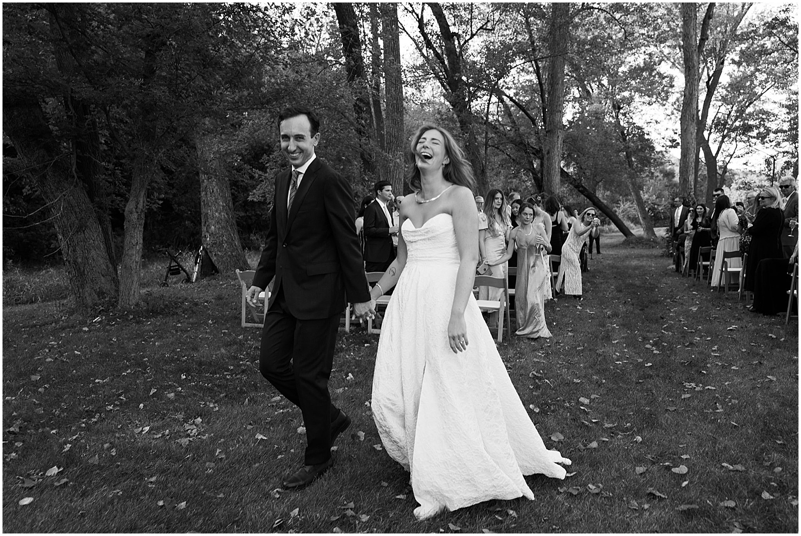 A bride and groom hold hands and laugh as they walk away from their Iowa City wedding ceremony.