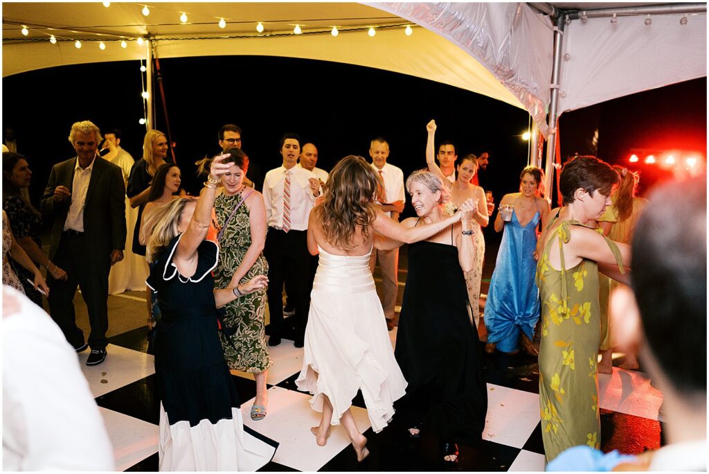 A bride dances with guests in a wedding tent.