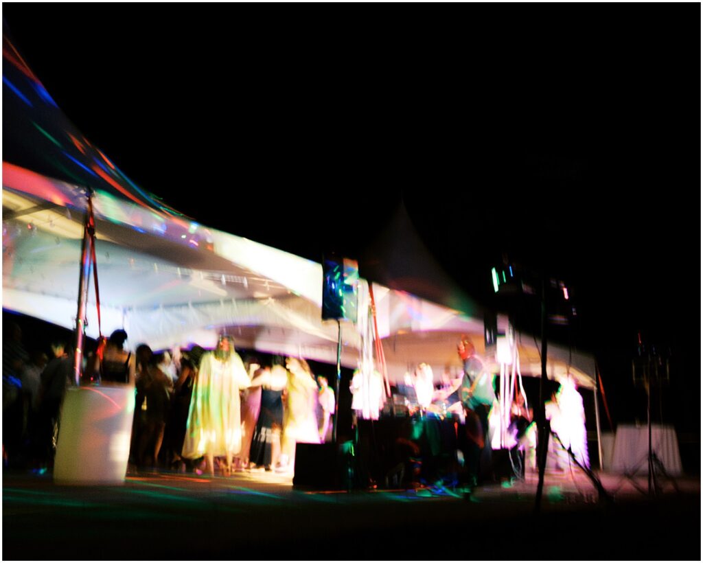 Wedding guests dance beneath a brightly lit tent at night.