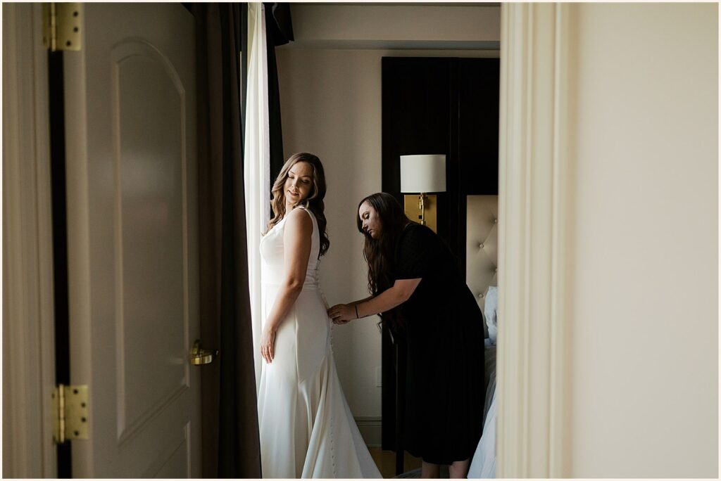 A bride's mother fastens her wedding dress in a hotel room.