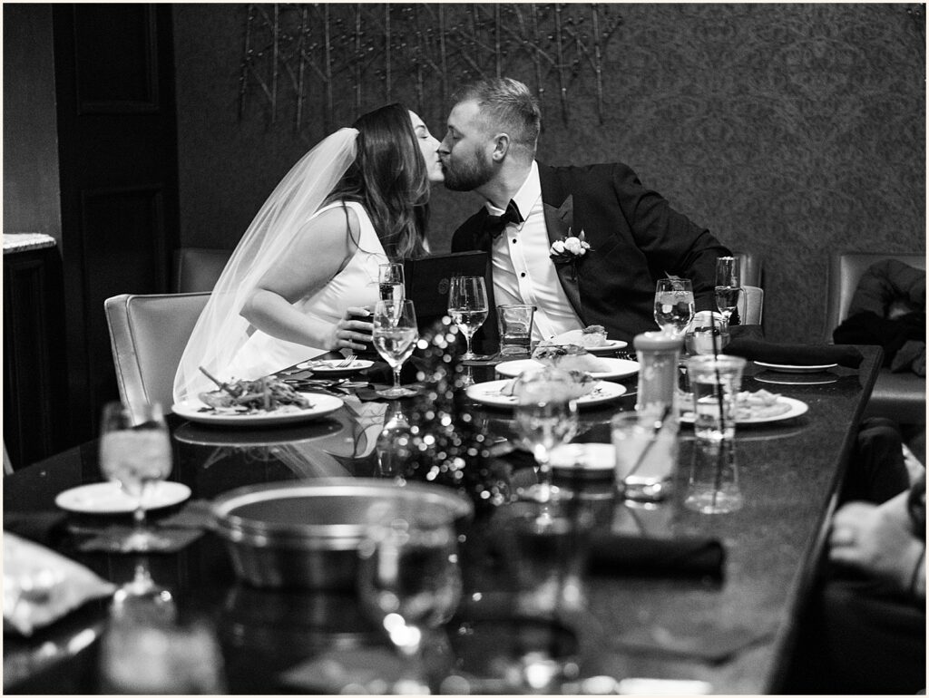 A bride and groom kiss at a dining table inside Hotel Blackhawk.
