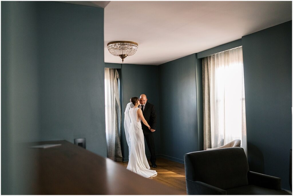 A bride and groom kiss in the corner of a Des Moines hotel room.