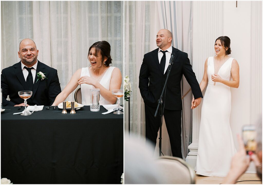 A bride and groom hold hands and laugh while they listen to a toast.