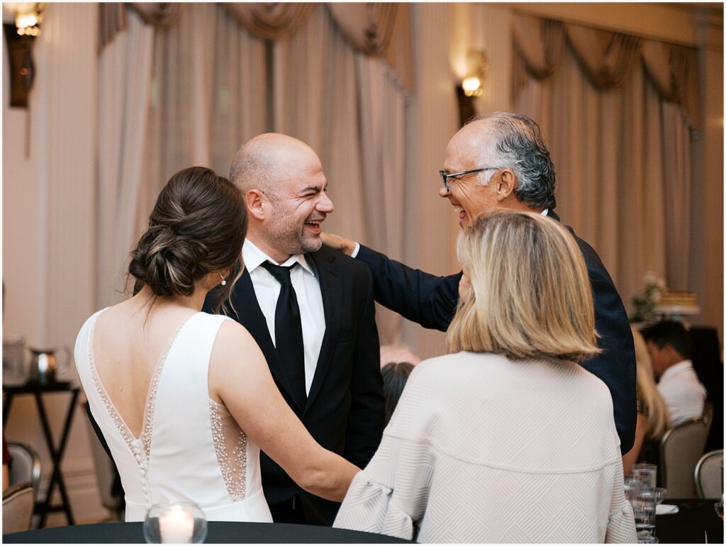 A bride and groom greet parents after a toast.