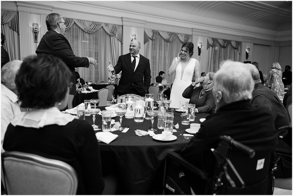 A bride and groom speak with friends sitting at a table during their wedding reception.