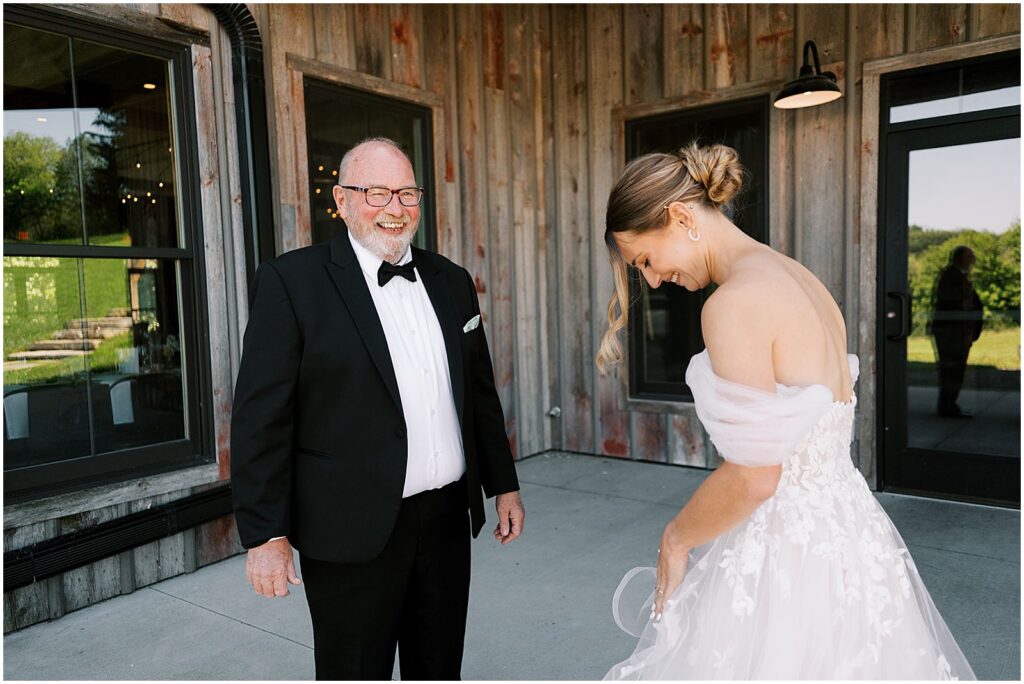 A bride shows her father her wedding dress on a porch at a wedding venue.