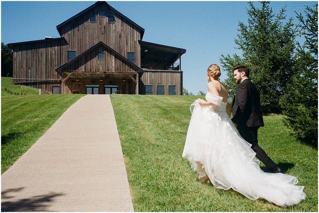 A bride and groom walk towards a wedding barn at Wilson's Ciderhouse in Iowa City.