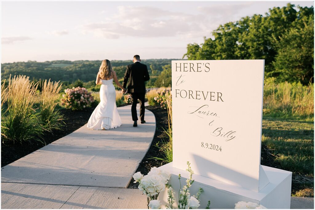 A bride and groom hold hands and walk down a path at Ashton Hill Galena.