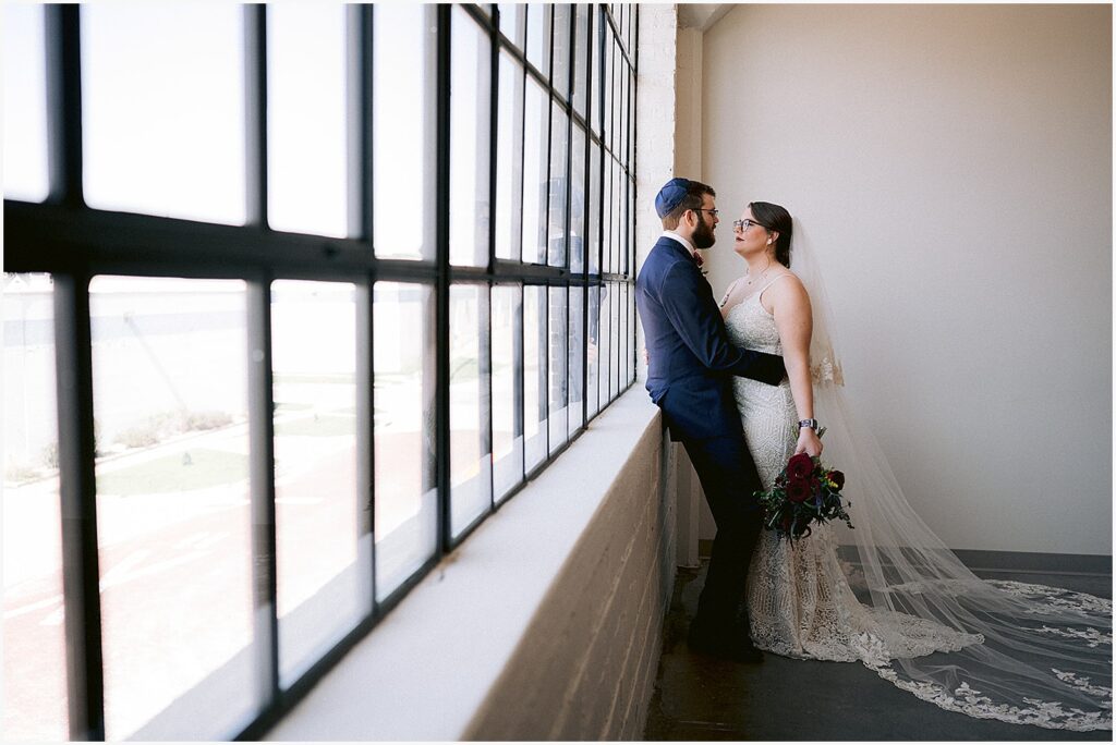 A bride and groom pose in front of a window at an Eastern Iowa wedding venue.