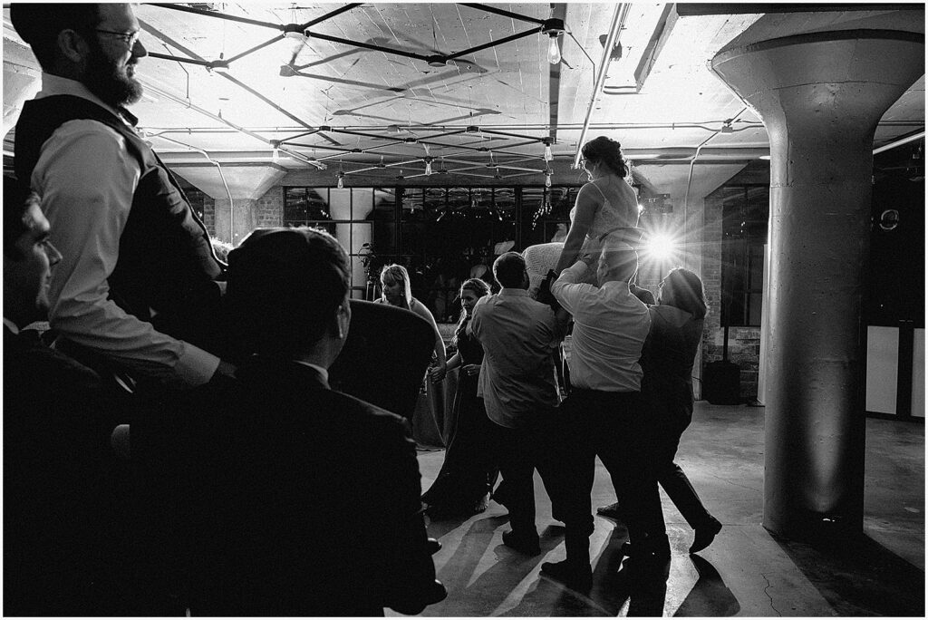 Wedding guests lift a bride in a chair for the hora.